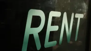 Užrašas „Rent“ ant tamsaus paviršiaus, simbolizuojantis būsto nuomos paieškas bei sutarties svarbą.