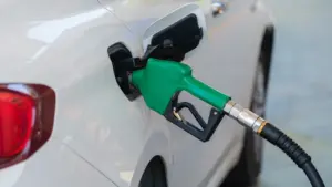 Degalų pistoletas įstatytas į balto automobilio kuro baką degalinėje.