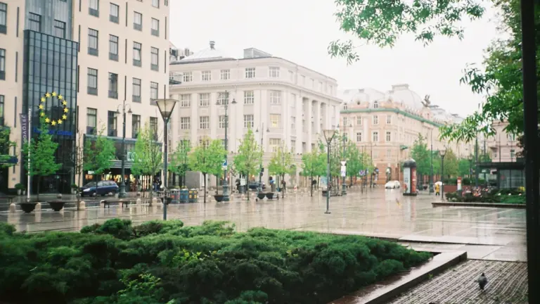 Lietingas Vilniaus miesto centras su pastatais ir šlapiais šaligatviais debesuotą dieną.