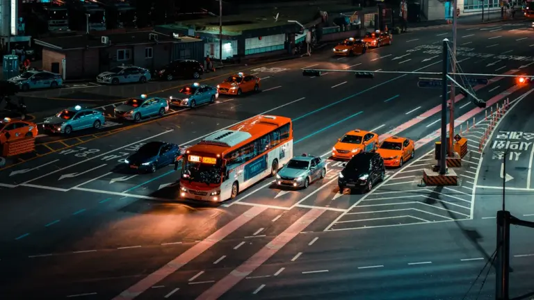 Viešojo transporto autobusas važiuojantis per naktinę Vilniaus gatvę su intensyviu eismu.