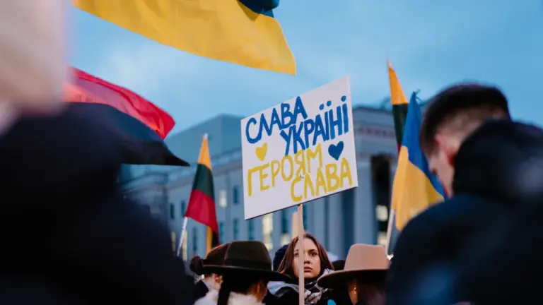 Žmonės Vilniuje dalyvauja mitinge, rodydami palaikymo Ukrainai plakatus ir vėliavas.