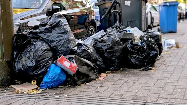 Dideli juodų šiukšlių maišų krūvos ant šaligatvio prie gyvenamųjų namų rajono
