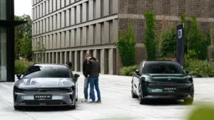 Du vyrai stovi šalia dviejų modernių „Zeekr“ automobilių šiuolaikinio pastato fone lauke.